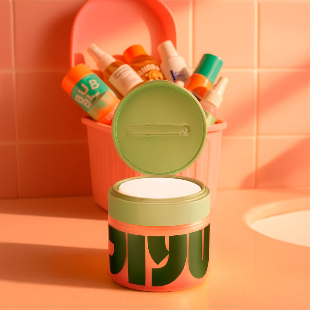 Open jar of toner pads with green flip lid on a bathroom counter, a caddy of assorted serum bottles behind it